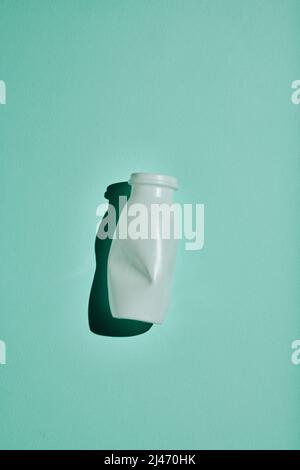 Vertical minimalistic flat lay shot of white plastic bottle on bluish green background, conscious consumption and recycling concept Stock Photo