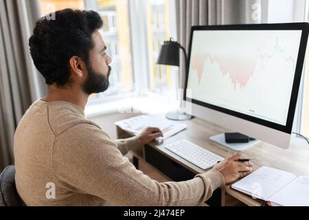 Concentrated man typing, messaging, indian programmer develops software, looks at computer screen. Focused hindu freelancer guy using computer in contemporary office space Stock Photo