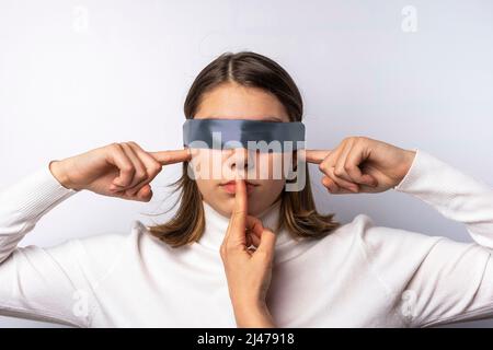 the girl covers her ears with her hands, her eyes are tied with a ribbon Stock Photo