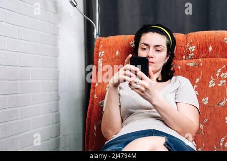 A middle-aged woman is sitting on the couch and using a smartphone  Stock Photo