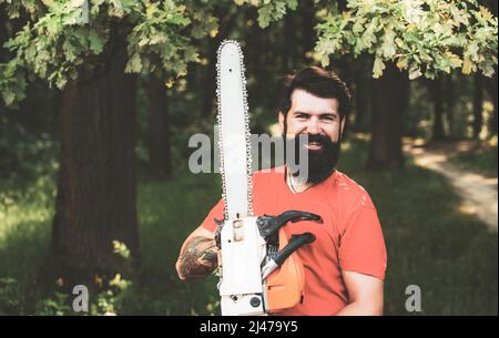 Stylish young man posing like lumberjack. Lumberjack worker standing in the forest with chainsaw. Deforestation. Stock Photo