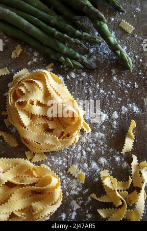 Italian cuisine. Homemade pasta pappardelle and asparagus isolated on wooden background. Directly above. Stock Photo