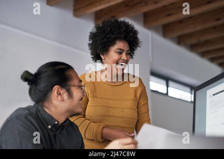 Laughing with coworkers is the best feeling. Cropped shot of two young businesspeople working on a computer together in the office during the day. Stock Photo