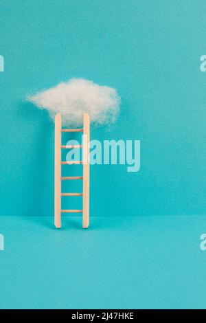 Ladder with a cloud on top, blue colored background, copy space, dreaming of success, creative and business concept, achieving new goals Stock Photo