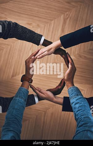 There is more power in unity than division. High angle shot of a group of unidentifiable businesspeople forming a circle with their hands. Stock Photo