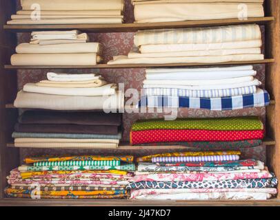 rustic wooden shelves filled with stacks of colorful colonial fabrics Stock Photo