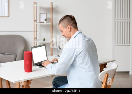 Young man using laptop on table with wireless portable speaker in room Stock Photo