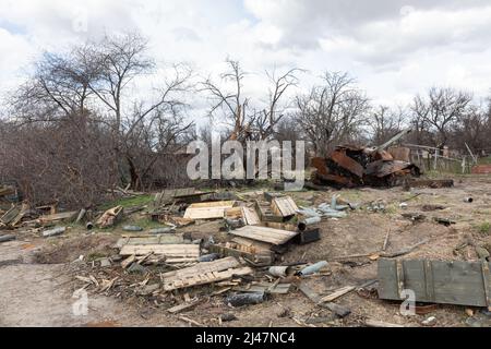 Burnt tank on the side of the road and other abandoned equipment, shells and empty boxes of weapons are lying in the middle of the field along the road near Andriivka after the retreat of Russian troops. Stock Photo