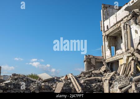 A ruined building with the remains of walls and a pile of concrete rubble against the background of the city and the blue sky. Background. Stock Photo