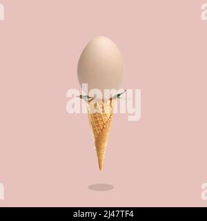Concept on the theme of Easter 2022, egg as a symbol of the holiday in an ice cream cone on a pink background with a shadow, postcard. Stock Photo