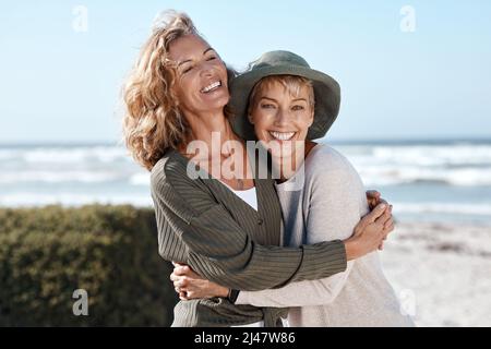 Best friends for life. Cropped shot of two attractive mature women hugging while standing on the beach. Stock Photo