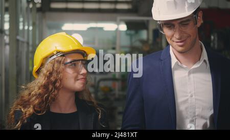 Caucasian maintenance engineer man and diverse female factory workers in hardhats walking on plant floor and talking, Manager supervisor and industria Stock Photo