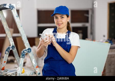 Positive young female contractor chatting online on smartphone Stock Photo