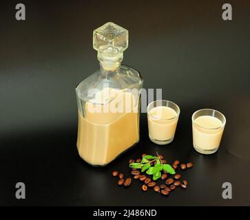 Creamy coffee liqueur, homemade alcohol with mint on a black background, a scattering of roasted cocoa beans nearby. Close-up. Stock Photo