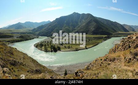 Panoramic shot of a bend in the bed of a beautiful river flowing through a valley around a high mountain in early autumn. Katun river, Altai, Siberia, Stock Photo