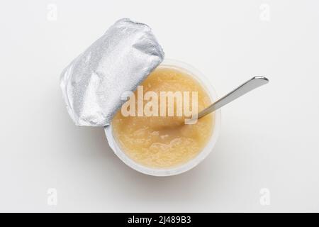 Top view of an opened cup of unsweetened applesauce with a spoon in it, isolated on a white background. Gluten-free vegan kids snack. Stock Photo