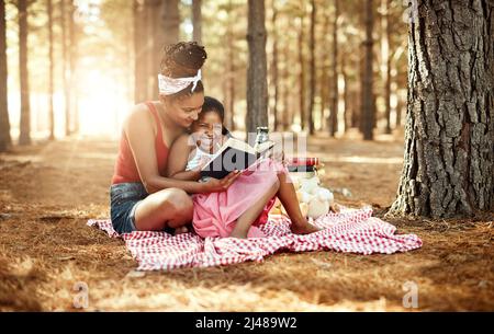 Spark your childs imagination and stimulate curiosity through reading. Shot of a mother and her little daughter reading a book together in the woods. Stock Photo