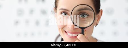 Woman optometrist holding magnifying glass in eyes against background of vision examination table Stock Photo