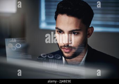 Data is my second language. Shot of a handsome young businessman sitting alone in the office at night and using his computer. Stock Photo