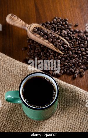 Green cup of coffee with coffee beans on wooden background Stock Photo
