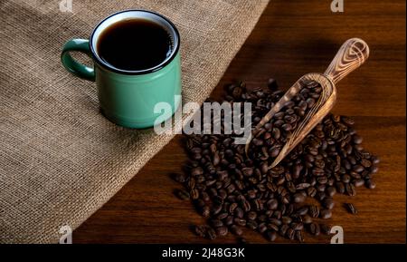 Green cup of coffee with coffee beans on wooden background Stock Photo