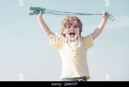 Portrait of cute boy exercising with jumping rope on blue sky background. Kid skipping rope during sunny morning. Stock Photo