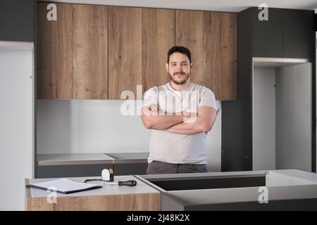 Young hispanic man smile and cross his arms after installing kitchen furniture. Stock Photo