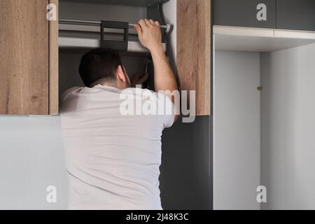 Young latin man installing an accessible kitchen cabinet in the kitchen. Stock Photo