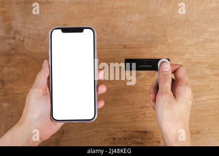 Hand holding mobile phone and hardware wallet on wooden table Stock Photo