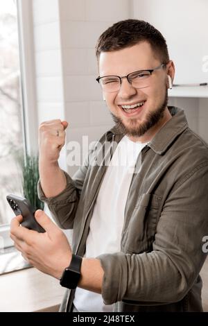 Happy young man looking at the camera, giving motivation to his co-workers while making a phone call, happy successful winner staying at home in the k Stock Photo