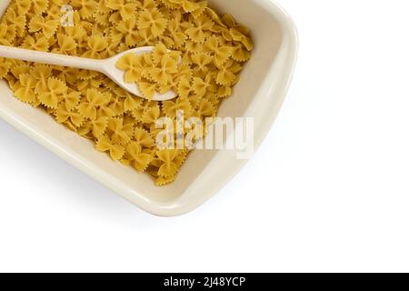 uncooked farfalle pasta in ceramic dish with wooden spoon and empty space for text isolated on white background, close-up, top view, concept of italia Stock Photo