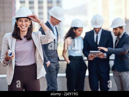 My team and I are ready to get your project started. Shot of a businesswoman wearing a hardhat while standing outside with her colleagues. Stock Photo