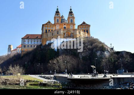 Melk, Austria - March 26, 2022: Unidentified people on bank of Danube River with impressive baroque Melk abbey on rock in UNESCO world heritage site o Stock Photo
