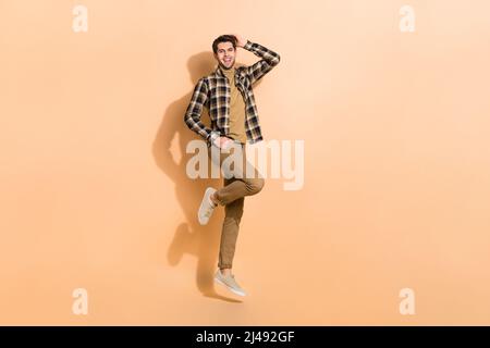 Full length body size view of attractive cheerful guy jumping posing having fun isolated on beige pastel color background Stock Photo
