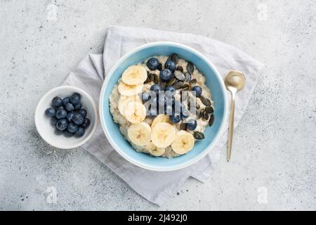 Healthy breakfast oatmeal porridge bowl with fruits and pumpkin seeds on grey concrete background. Top view Stock Photo