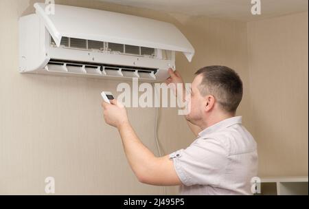 A home appliance repairman repairs the air conditioner, holds a remote control in his hand Stock Photo