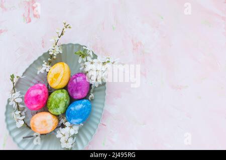 Colorful Easter eggs on plate and spring white cherry blossom flowers on pink background. Easter celebration concept. Top view, flat lay, copy space Stock Photo