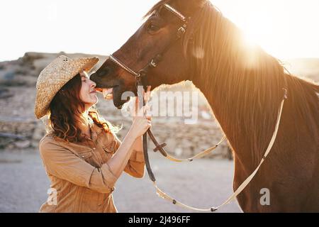 Young farmer woman having tender moment kissing her horse at farm ranch - Focus on face