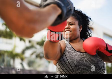 African curvy woman and personal trainer doing boxing workout session outdoor - Focus on face Stock Photo