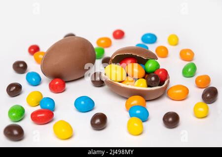 Half of a cracked chocolate egg filled with multi-colored candies covered with an egg shell on a white background with multi-colored candies. Treats f Stock Photo
