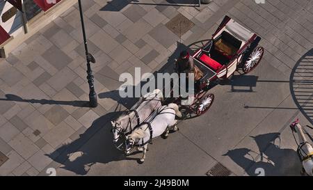 High angle view of a fiacre, a horse-drawn four-wheeled carriage, in the historic center of Vienna, Austria on sunny day with shadows. Stock Photo
