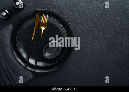 Ceramic empty black plate, silverware and linen kitchen towel napkin on old black ceramic cement concrete table background. Cooking stone backdrop. To Stock Photo
