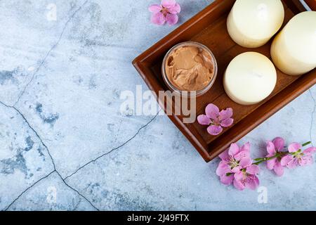 Glass cosmetic  jar of cream, decorative flowers and candles on a tray on a marble background. Natural organic cosmetics. Spa products for health and Stock Photo