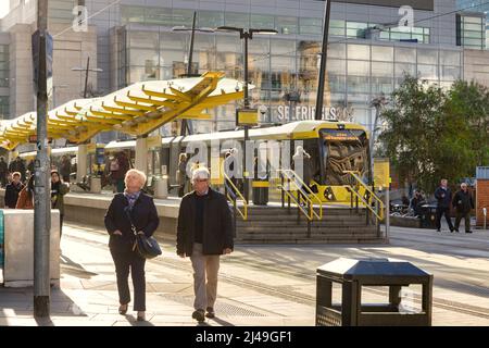 2 November 2018: Manchester, UK - Metrolink tramstop in Exchange Square, senior couple walking away, winter sunshine.