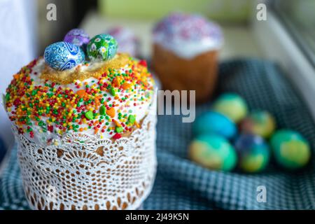 Three traditionally baked orthodox easter cakes with glace icing and bright blue and yellow flowers on wooden background with lace fabric and red cand Stock Photo