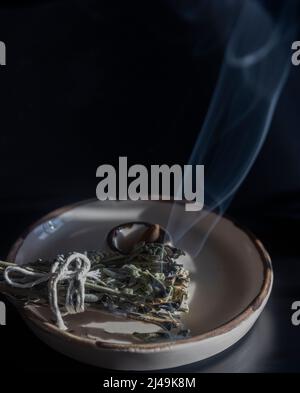 Smoke on dark background from burning sage herb, standing on a ceramic incense holder, selective focus Stock Photo