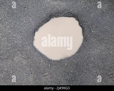 Hole and puddle on bad broken road. destroyed Road with Puddle. Bad road. Puddles and dirt on dirt road. Stock Photo