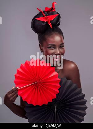 Got to have tons of red in my life. Studio portrait of a beautiful young woman wearing Asian inspired makeup and posing with origami against a grey Stock Photo