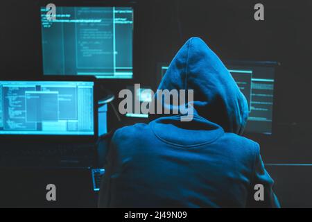 Hacker using computer for organizing massive data breach attack on goverment servers. Hacker in dark room surrounded computers Stock Photo