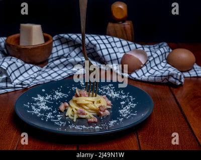 A plate of carbonara-style rolled spaghetti, with a fork skewered on top Stock Photo